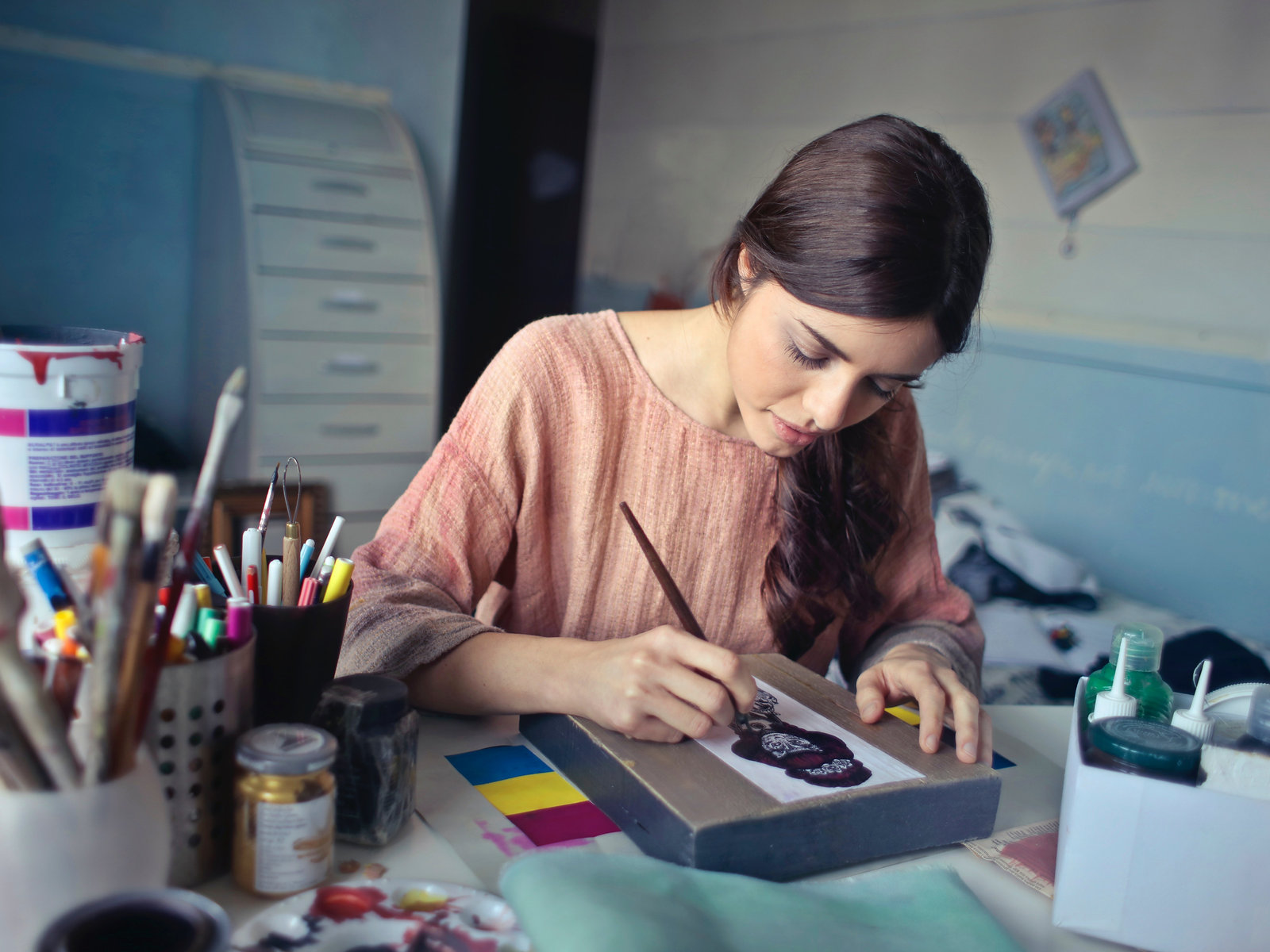 Margit Avelane painting at her desk in a bright studio