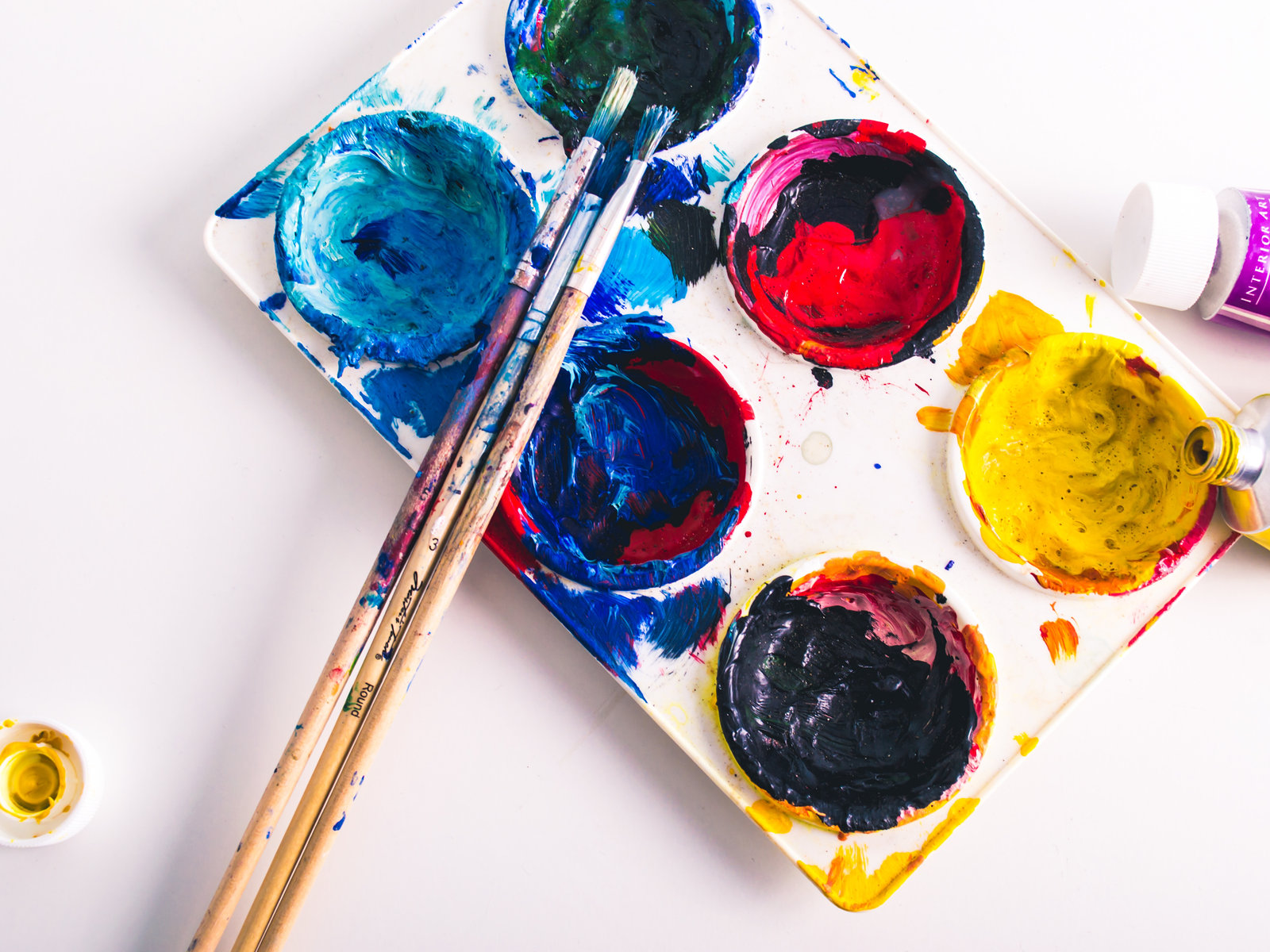 A white palette with bright wells of blue, red and yellow paint, and two brushes