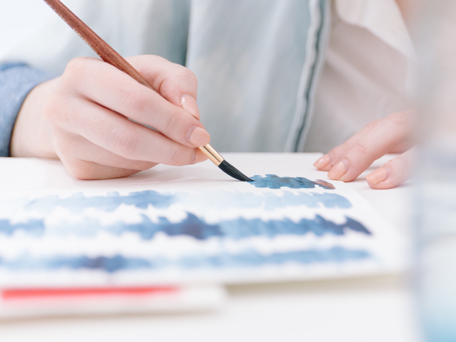 A hand laying a stroke of blue watercolor across white paper